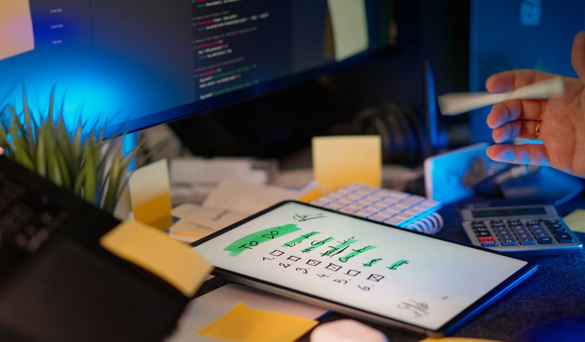 A to-do checklist on a tablet beside code on a screen